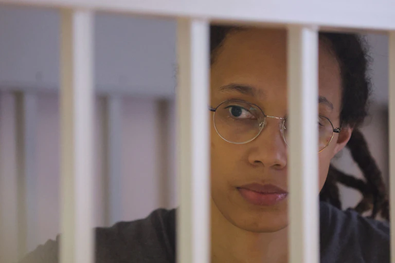 Brittney Griner, looks plaintively through white bars.