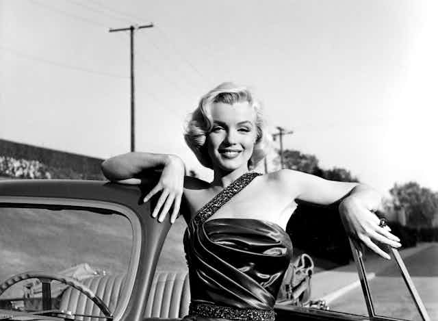 Marilyn Monroe apoyada en un coche descapotable.