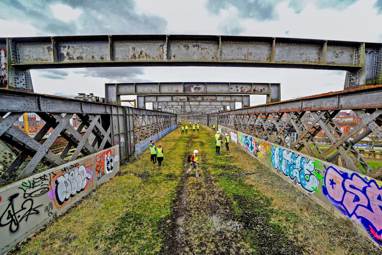 An old railway bridge seen from up high with workmen in high-vis vests.