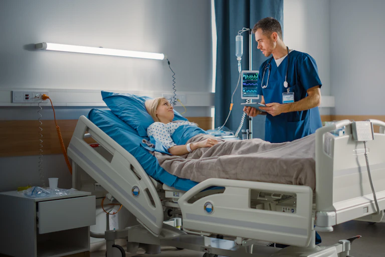 A young woman in a hospital bed speaks with a young male nurse.