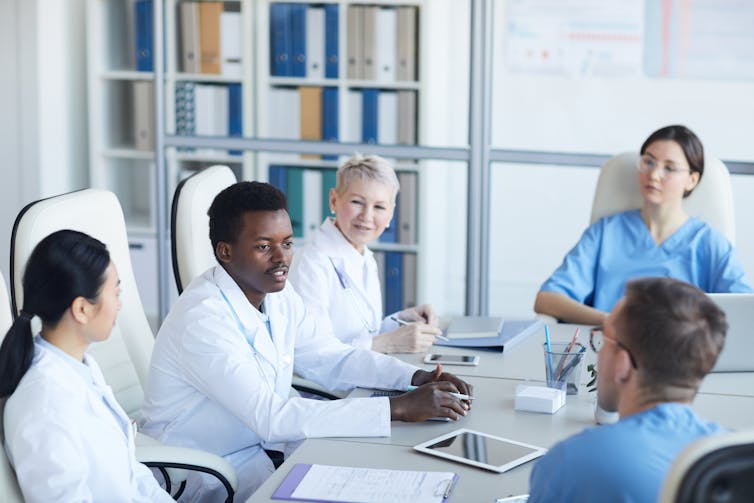 A group of five doctors and nurses have a discussion while seated at a conference table.