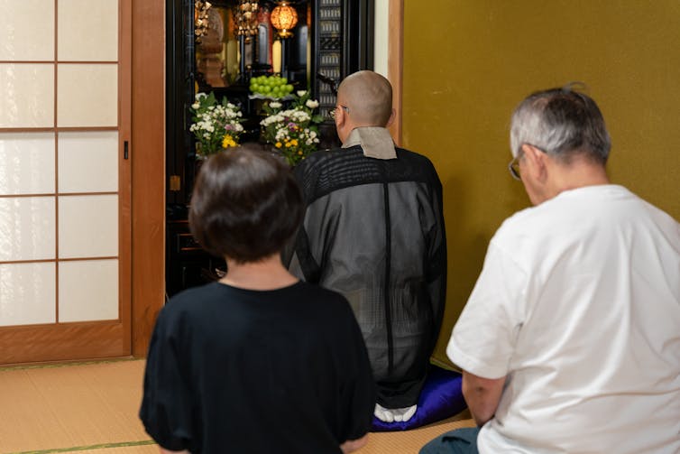 An older couple seen from behind with a monk and an altar.