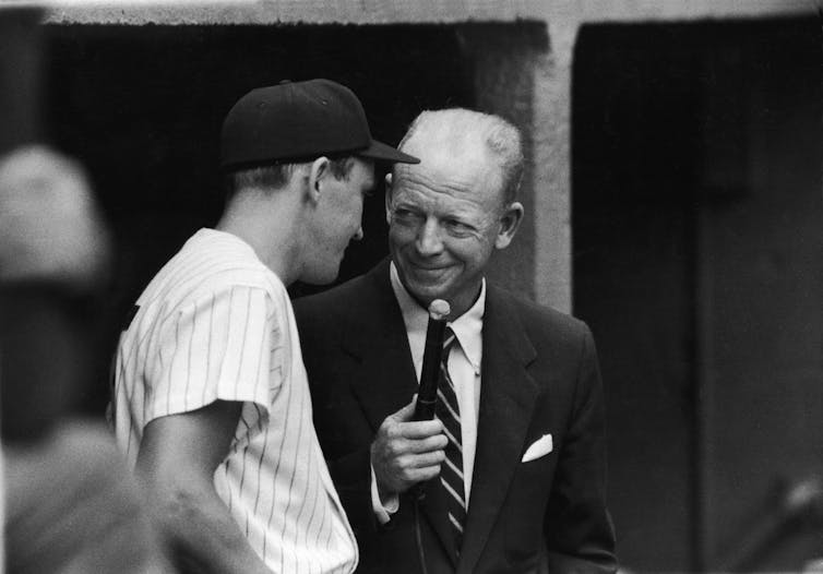 Man holding microphone interviews baseball player.