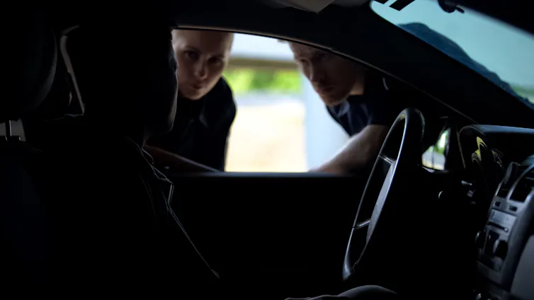 Two police officers question a man in a car.