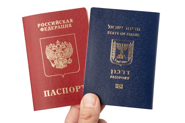 A person holds a red Russian passport and a blue Israeli passport against a white background.