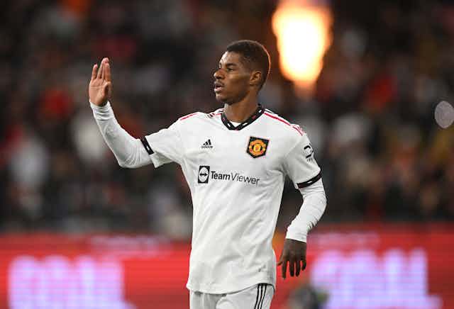 Marcus Rashford in white football kit with his hand raised for a high five