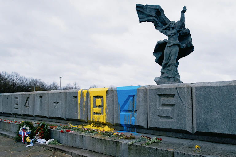 Statue of a woman on a wall with war dates, splashed with yellow and blue paint