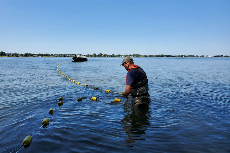 homme déploie un filet dans l'eau avec bateau au loin