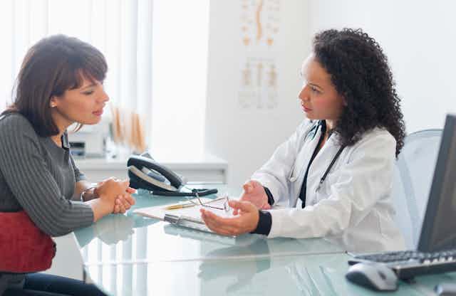 A female patient sits across a table conversing with a female physician.