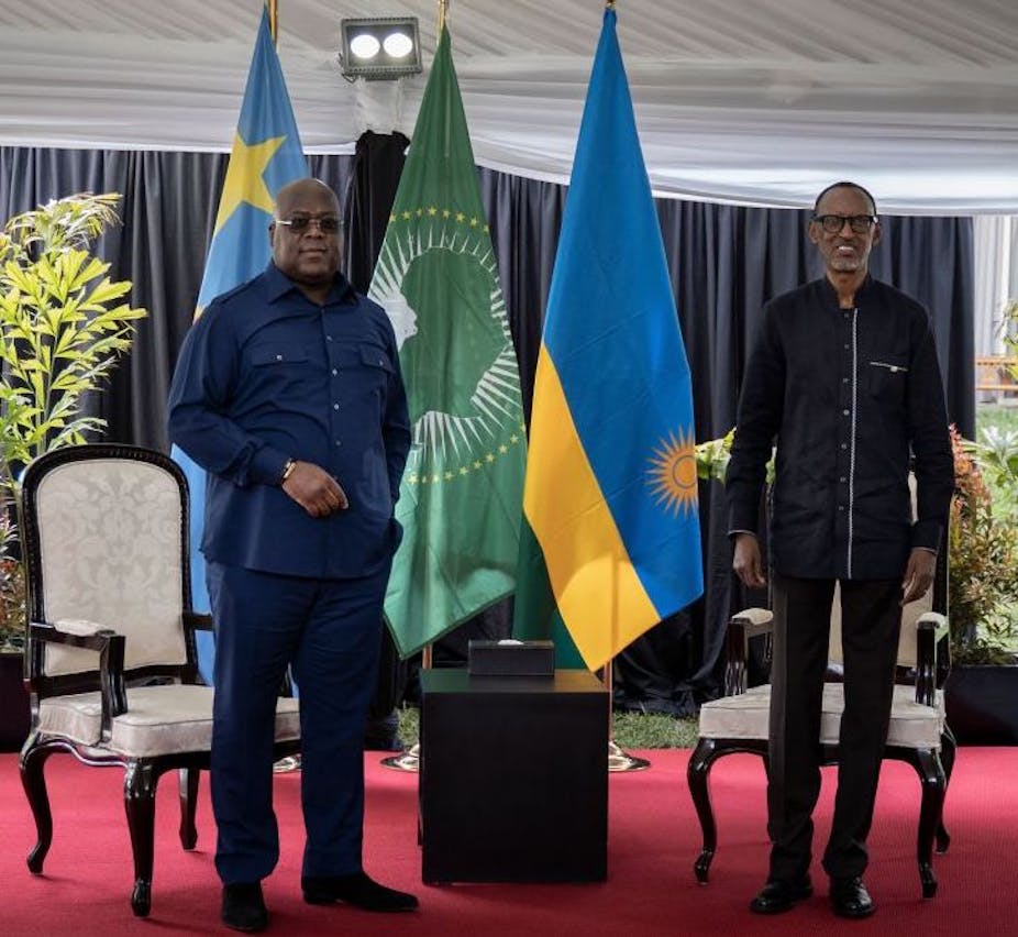 Men standing on stage with Rwanda, Congo and African Union flags behind them.