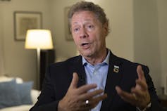 A man with curly brown hair gestures as he speaks.