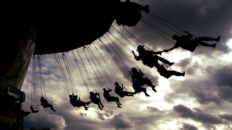 A contraluz, un grupo de adultos disfruta de una atracción con columpios en un festival de música.