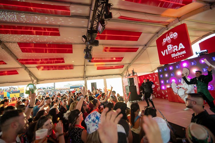 Un grupo de personas bota junto a un cantante que actúa en el escenario de una carpa patrocinada.