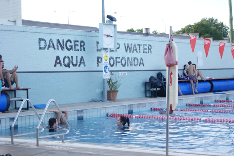 swimmers in the Fitzroy Pool, with the words 'AQUA PROFUNDA' (deep water) on the wall behind them