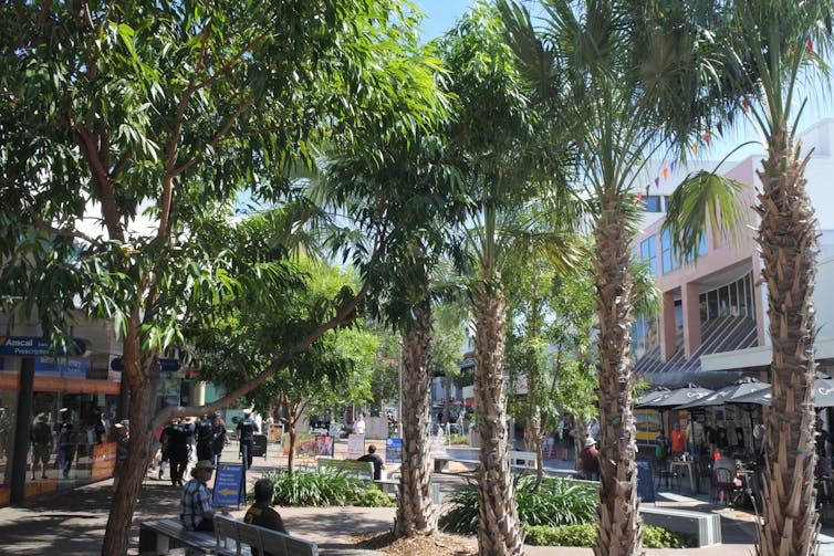 people sit and walk through leafy shopping street