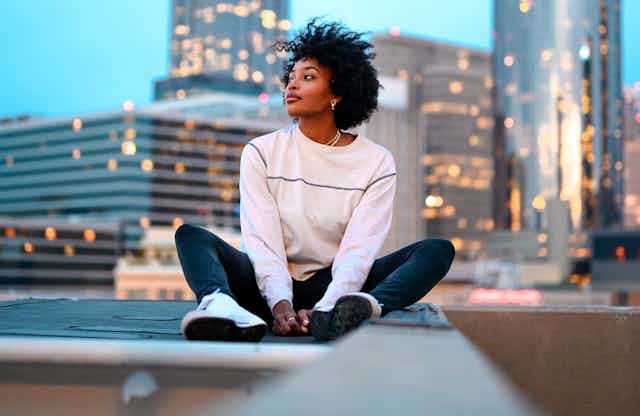Woman sits on city rooftop, thinking.