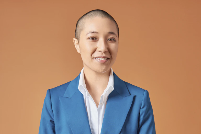 a smiling nonbinary person with a shaved head, in a blue suit and white shirt