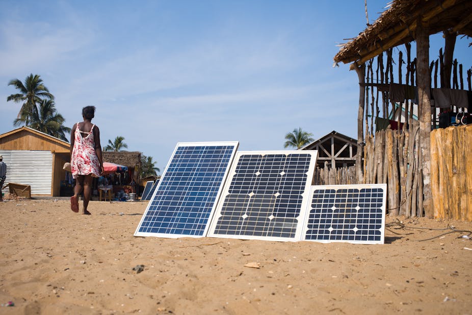 Woman wearing dress walking next to three solar panels propped up on the sandy floor.