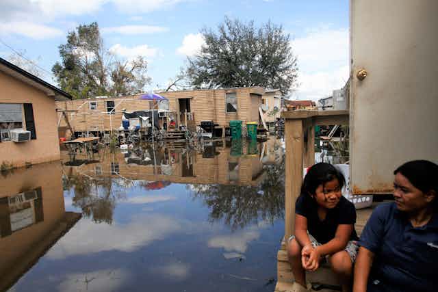 Una mujer y un niño sentados en las escaleras de una casa en un barrio inundado y destruido por el huracán.