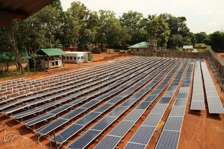 A ground-mounted solar power plant in a small community with a forest in the background.