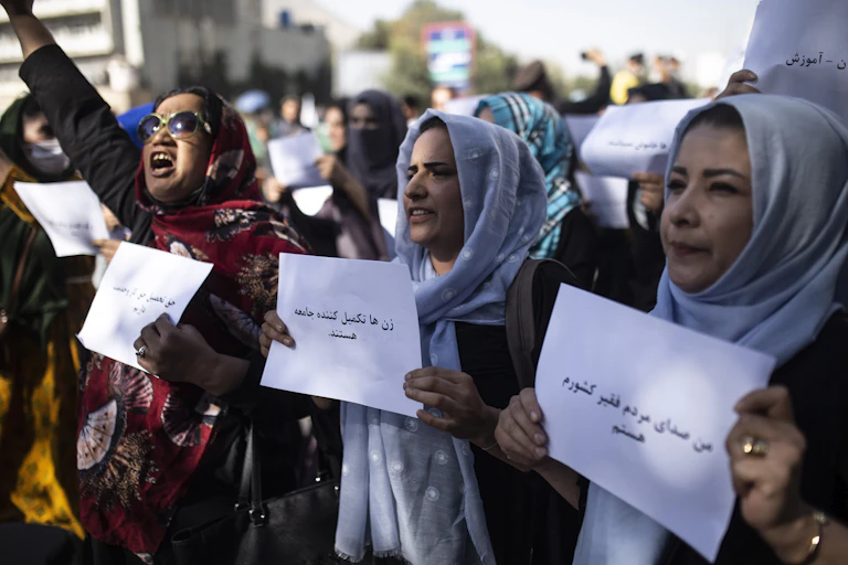 Three women hold up signs, one with her arm raised and shouting.