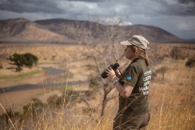 A person holding binoculars looks out over an African savannah.