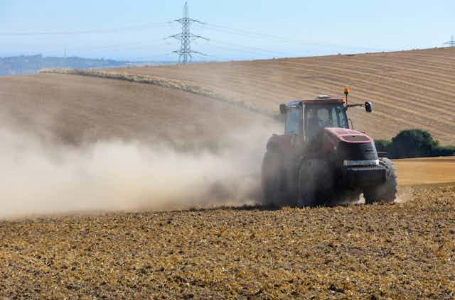 A red tractor throws up dust as it crosses a dry farm field.