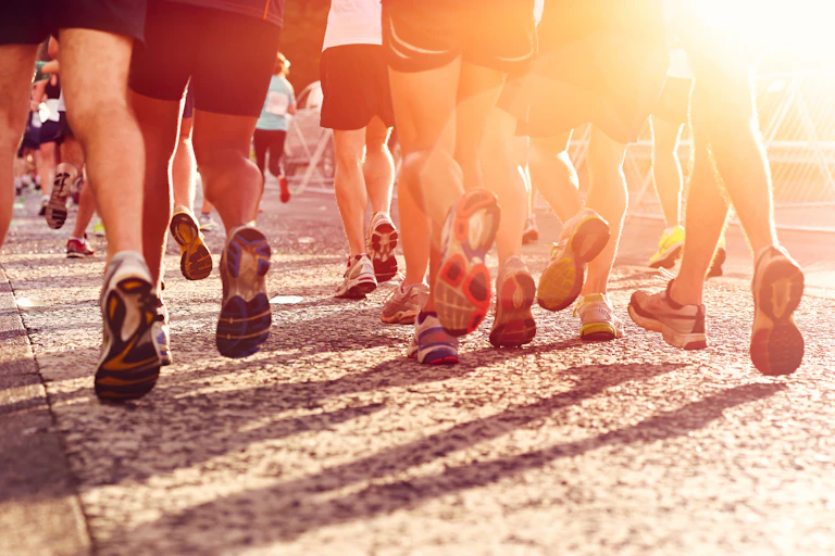 Cropped photo of runners from behind, showing legs and running shoes in strong sunlight