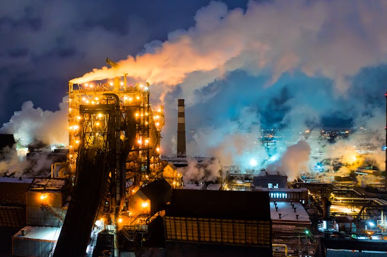 A metallurgical plant at night with chimneys belching smoke.