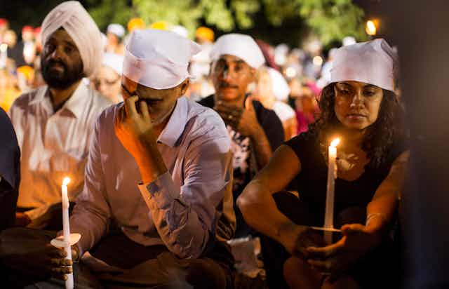 Three men and one woman wearing white turbans and holding candles.