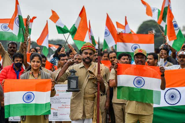 Indians stand in a crowd facing the camera, all holding the tricolor flag