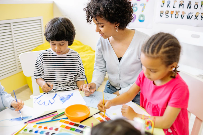 A teacher seen with young children at a table.