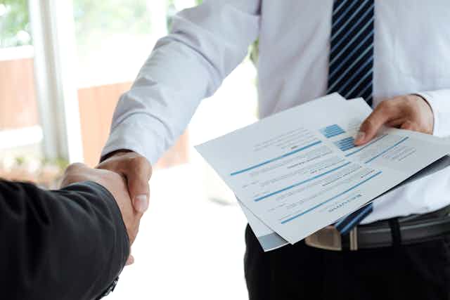 A man holding a resume and shaking the hand of someone off-camera