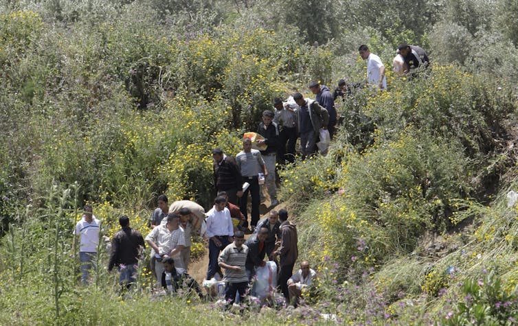 People toting their belongings walk through grassy hills.