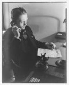 A vintage black and white photograph of man seated at a desk holding a telephone receiver to his head