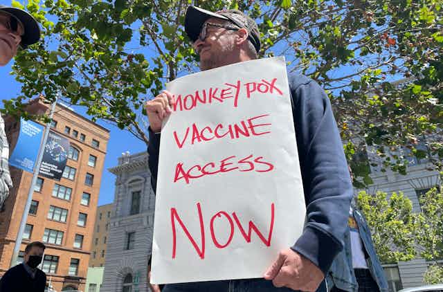 Man holding sign at protest demanding monkeypox vaccine