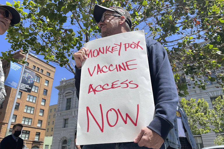 Man holding sign at protest demanding monkeypox vaccine