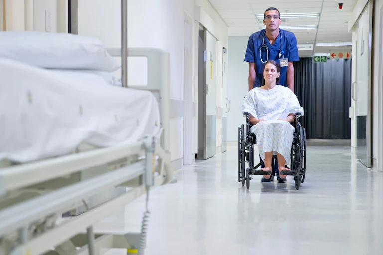 woman pushed in wheelchair in hospital corridor