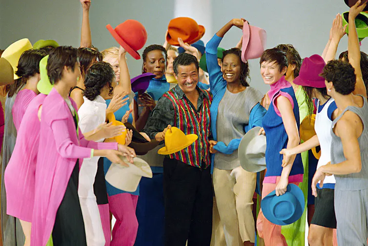 Models in colorful clothes surround Japanese designer Issey Miyake