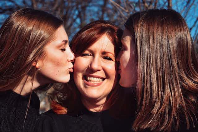 Two grown up daughters kissing their mum on the cheek