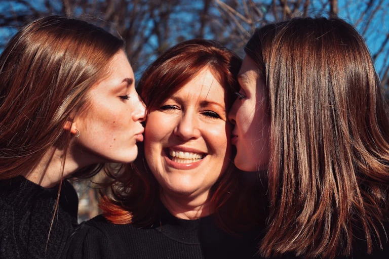 Two grown up daughters kissing their mum on the cheek