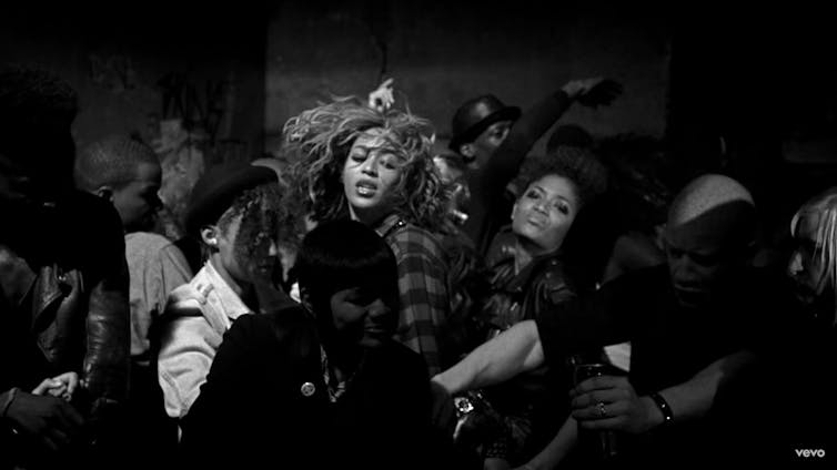 En un fotograma en blanco y negro, Beyoncé baila en medio de un grupo de gente.