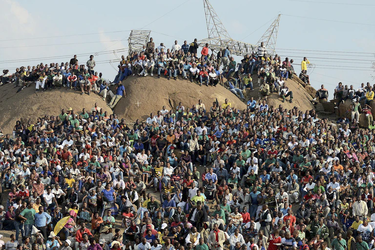 Hundreds of men ands women sit or stand on a hilltop.