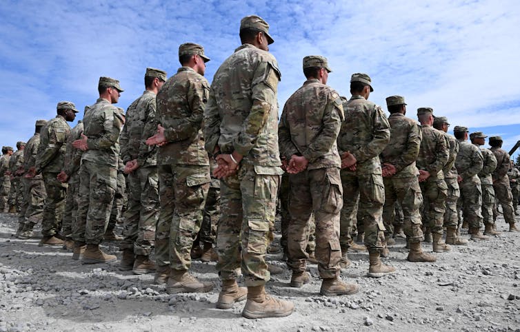 Dozens of soldiers dressed in uniforms form a square and stand at attention.