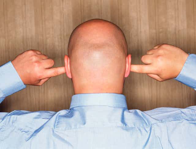 back of a man's shaved head, holding his fingers in his ears