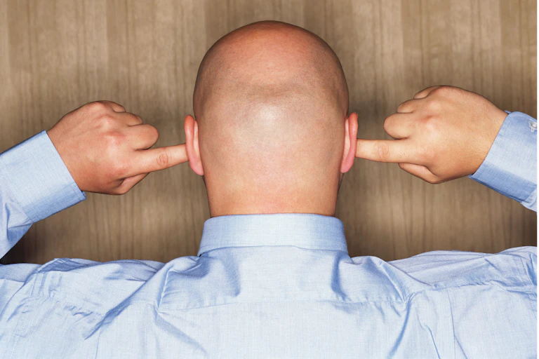 back of a man's shaved head, holding his fingers in his ears