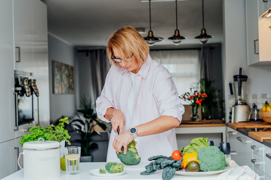 A middle-aged woman cuts broccoli on her kitchen countertop.
