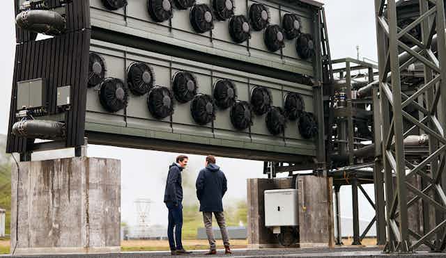 Climeworks Orca plant in Iceland with founders standing in front of a large piece of equipment, about the height of a 2-story house, with fans