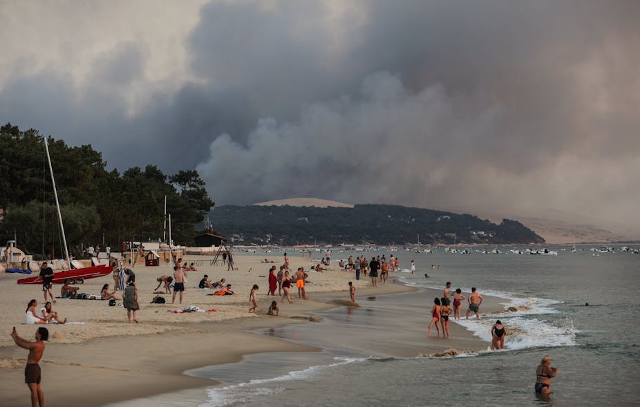 Personnes se baignant sur la baie d'Arcachon tandis qu'un feu géant recouvre les Landes au loin