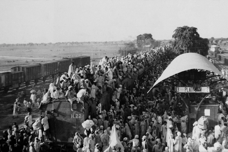 Hundreds of people gathered at a train station, with some sitting on top of a coach.